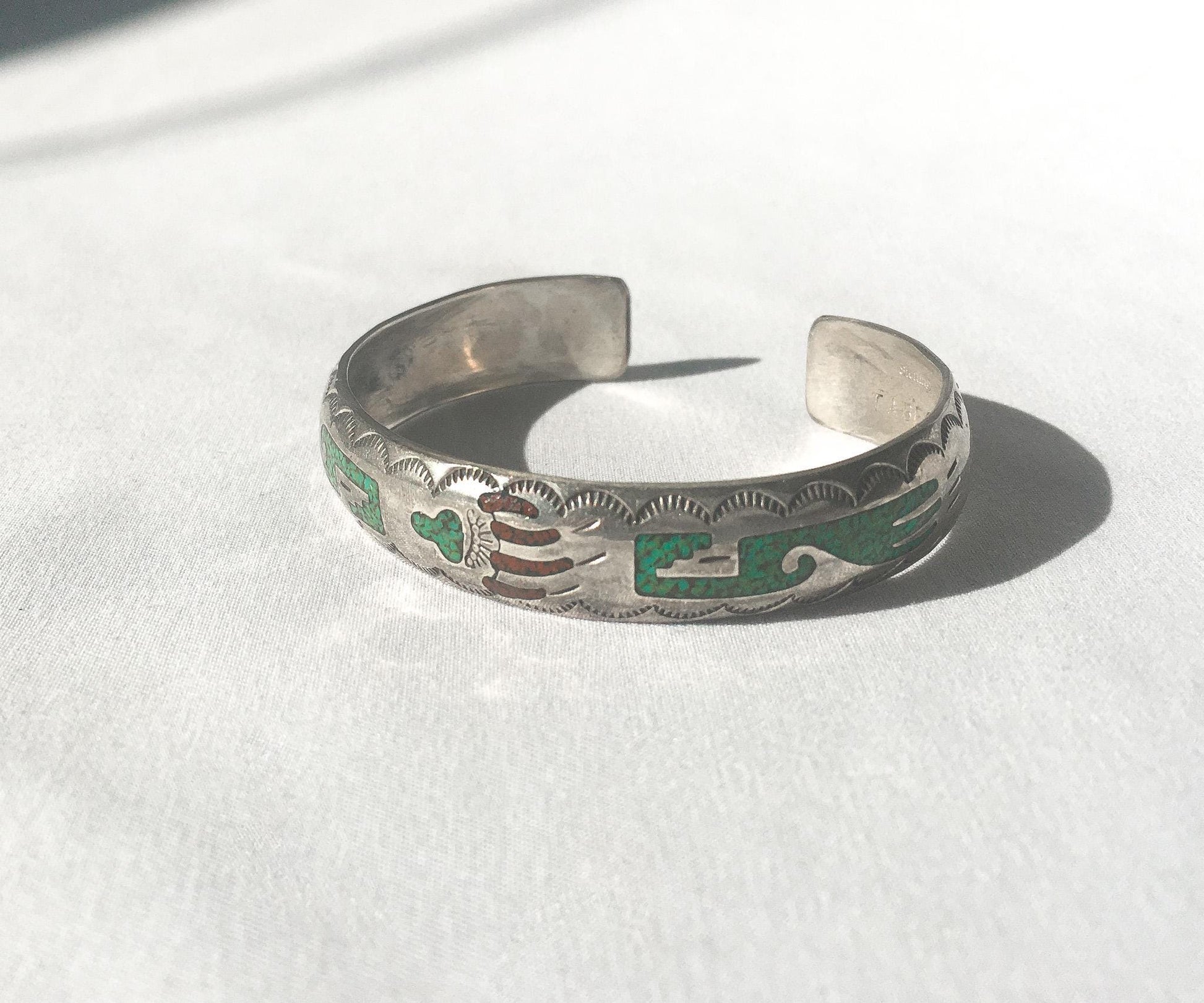 May include: A silver bracelet with a green and red inlay design. The bracelet is made of sterling silver and has a traditional Native American design.