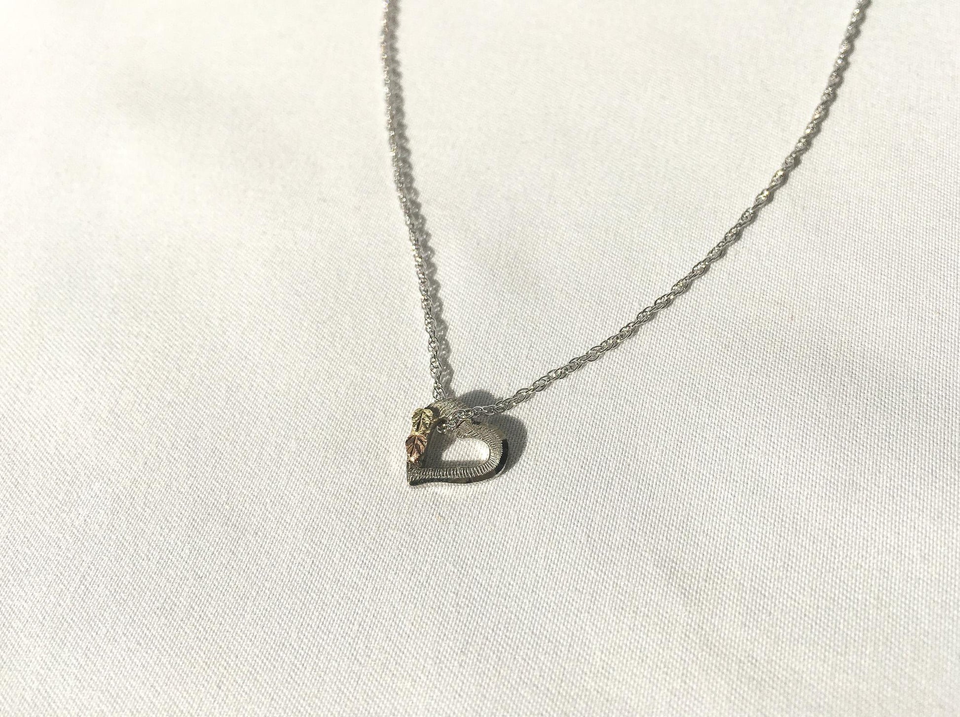 May include: A silver chain necklace with a heart-shaped pendant. The pendant has a small gold accent on the top.