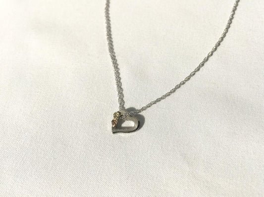 May include: A silver chain necklace with a heart-shaped pendant. The pendant has a small gold accent on the top.