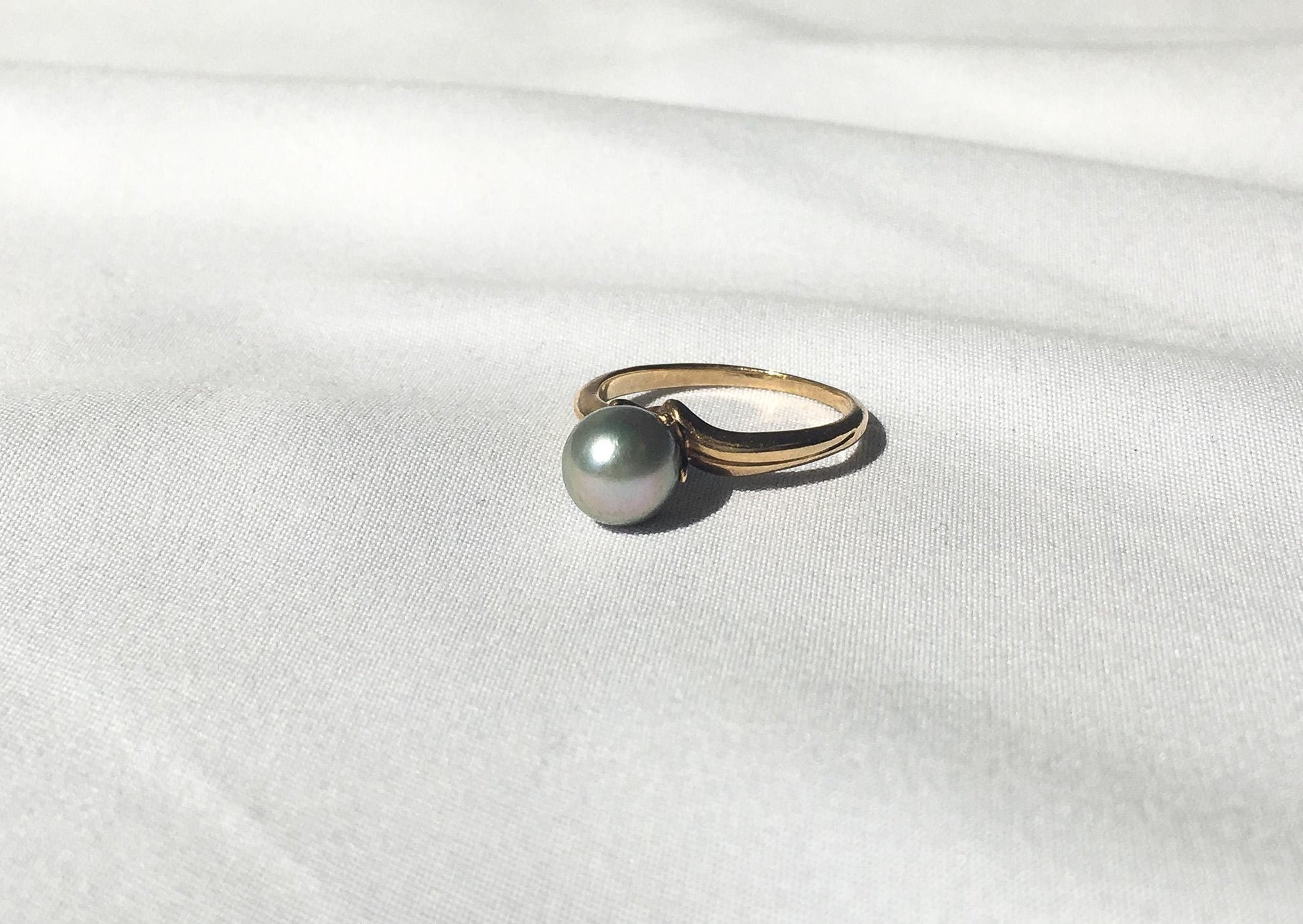 May include: A gold ring with a single gray pearl set in the center.