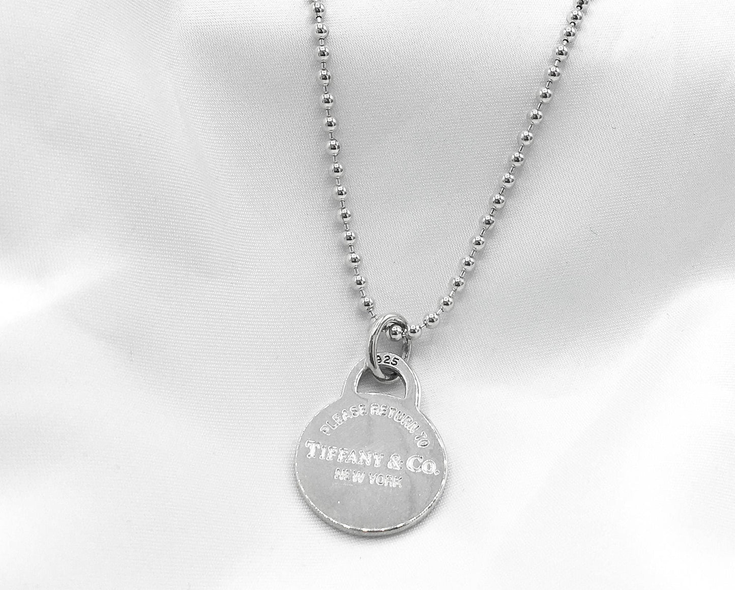 May include: A silver necklace with a round pendant that reads 'Tiffany & Co. New York'.