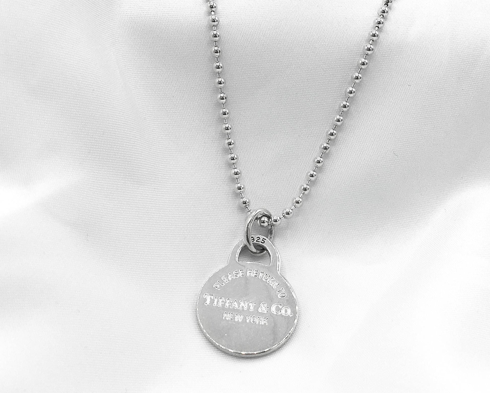 May include: A silver necklace with a round pendant that reads 'Tiffany & Co. New York'.