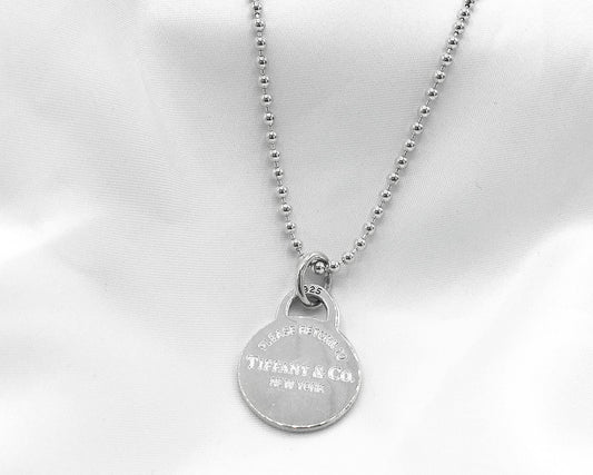 May include: A silver necklace with a round pendant that reads 'Tiffany & Co. New York'.